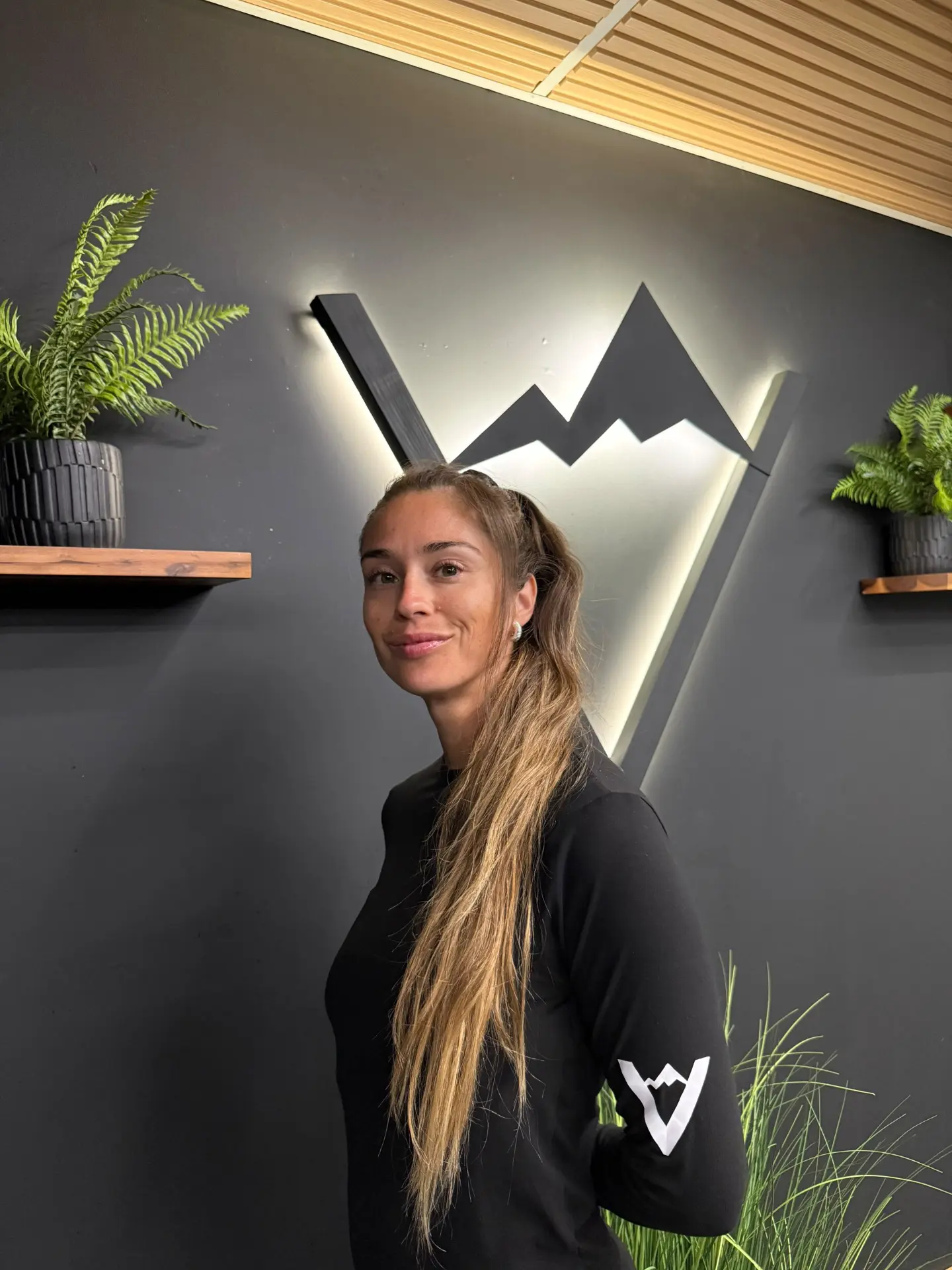 Daniela in a Valley Studio top standing beside the illuminated mountain logo
